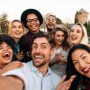 Friends chilling outside taking group selfie and smiling. Laughing young people standing together outdoors and taking selfie.